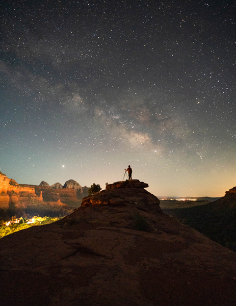 Person on top of rock formation under starry sky